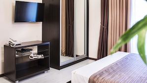 Una habitación de hotel moderna con cama, televisor montado en la pared, armario y escritorio con teléfono y control remoto.