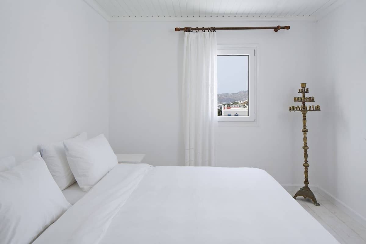 A bedroom with a large bed, a nightstand, a window with a view, and a tall floor lamp.