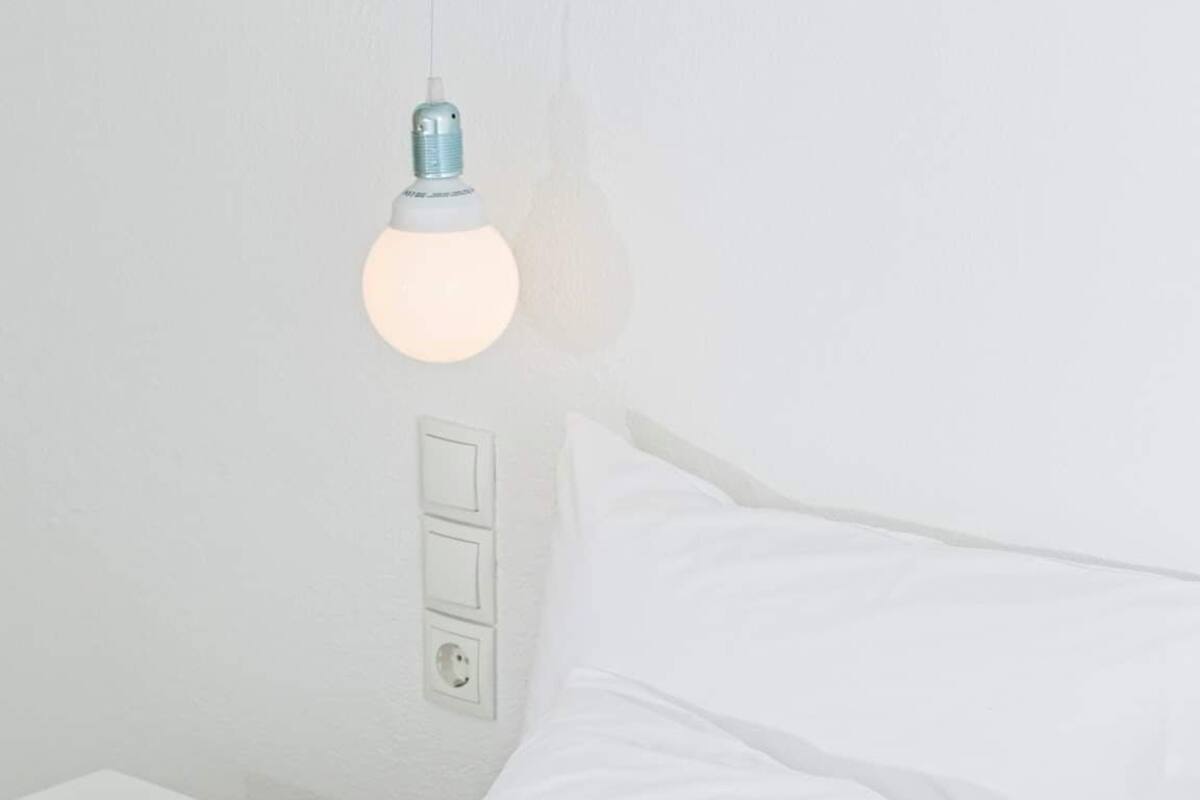 A neatly made bed with white bedding and pillows, a tablet on the bed, and a hanging light fixture above.