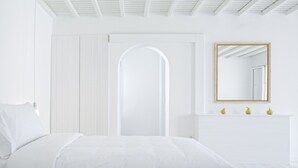 Un dormitorio blanco con cama, armario, espejo y cómoda con tres objetos decorativos.