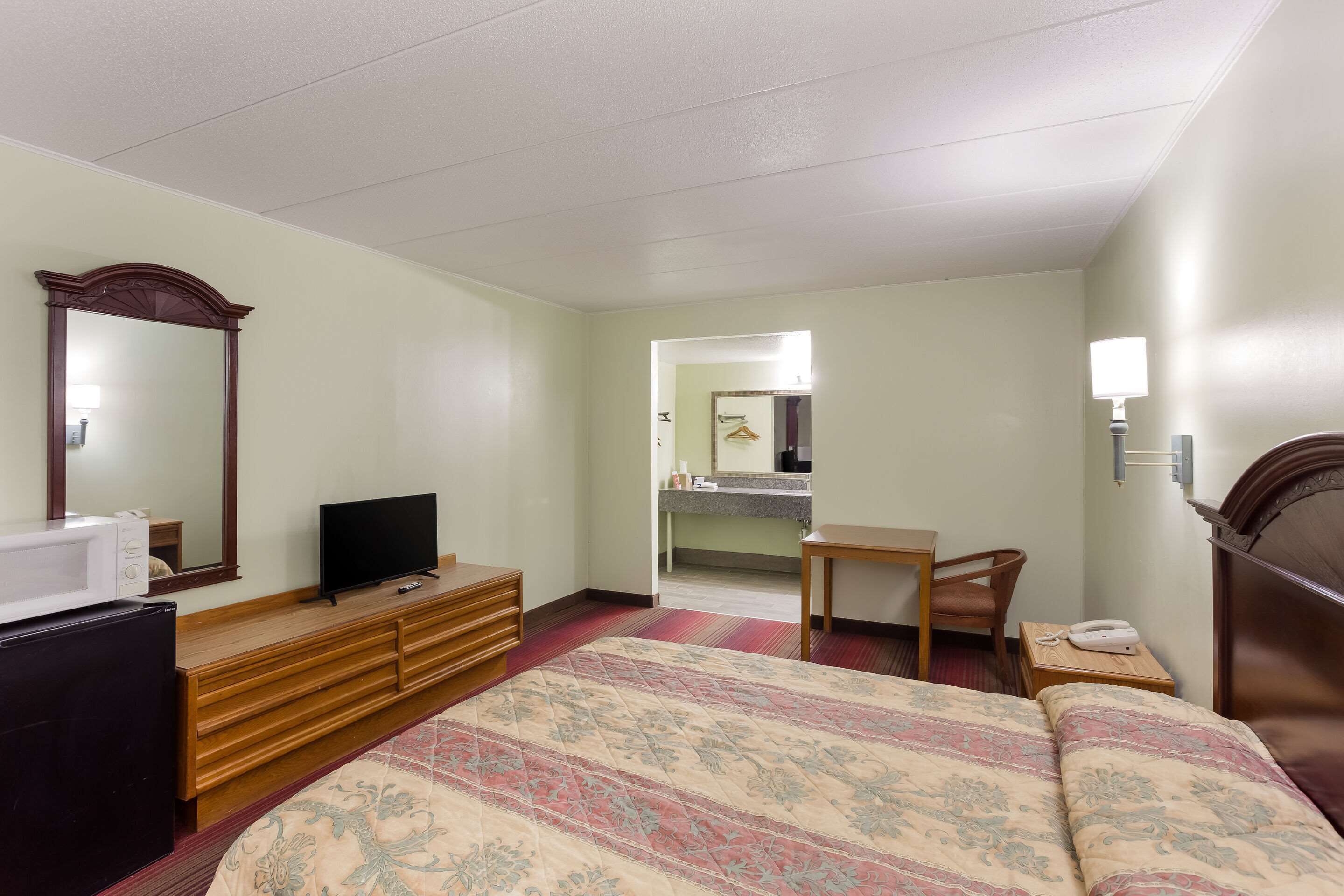 A hotel room with a bed, a dresser, a television, a desk, and a mirror.