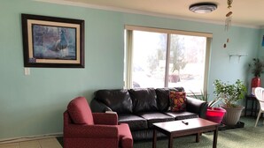 A living room with a black leather sofa, a red armchair, a wooden coffee table, and a large window with a view of the street. - Rodeway Inn South Point (South Point)
