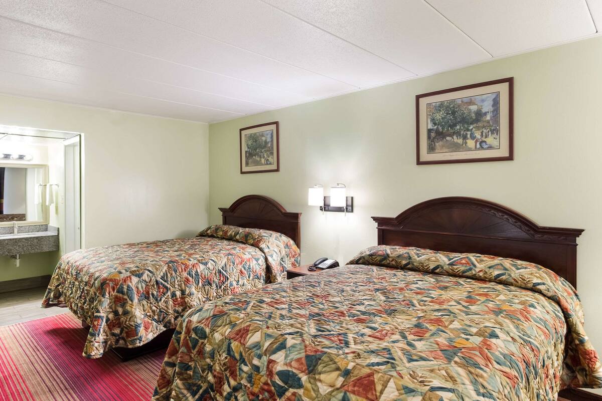A hotel room with two beds, a bathroom with a sink, and two framed pictures on the wall.