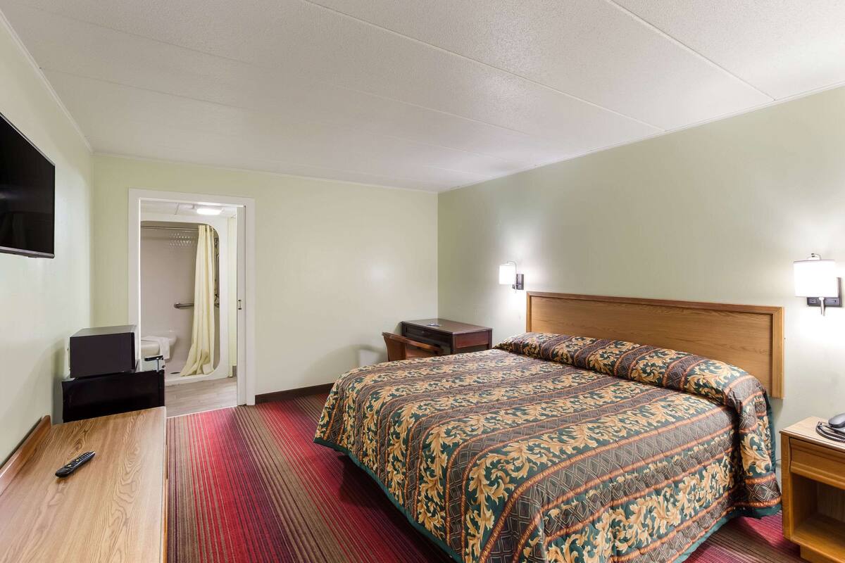 A hotel room with a large bed, a wooden headboard, a flat-screen TV, a bedside table, and a nightstand.