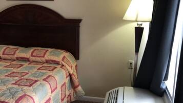 Habitación de hotel con cama, aire acondicionado de pared, lámpara y un cuadro enmarcado.