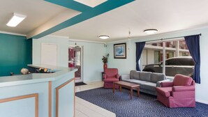 A reception area with a counter, a red armchair, a grey sofa, and a patterned blue carpet. - Rodeway Inn South Point (South Point)