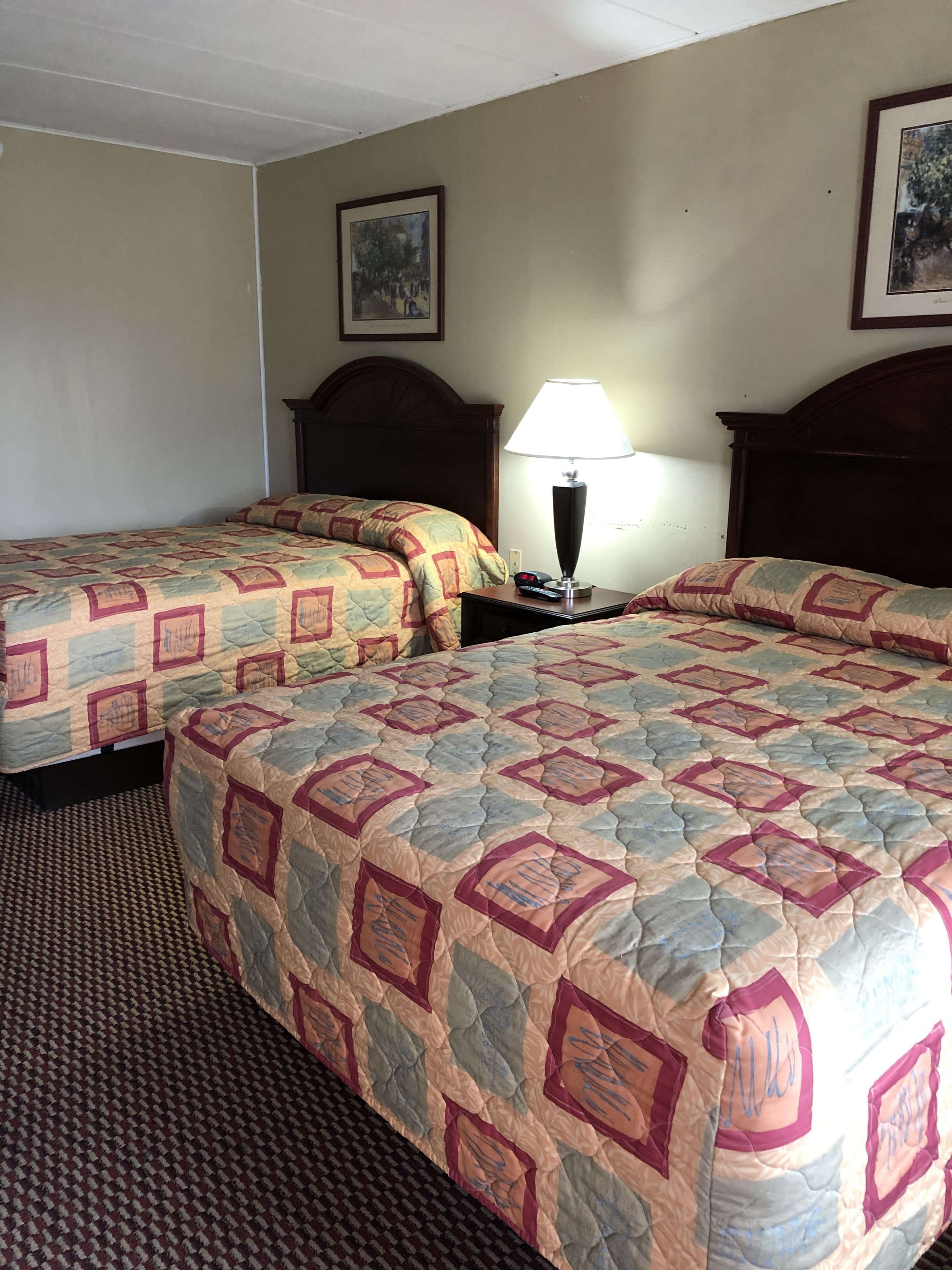 Une chambre d’hôtel avec deux lits, une table de chevet avec une lampe et un tableau encadré au mur.