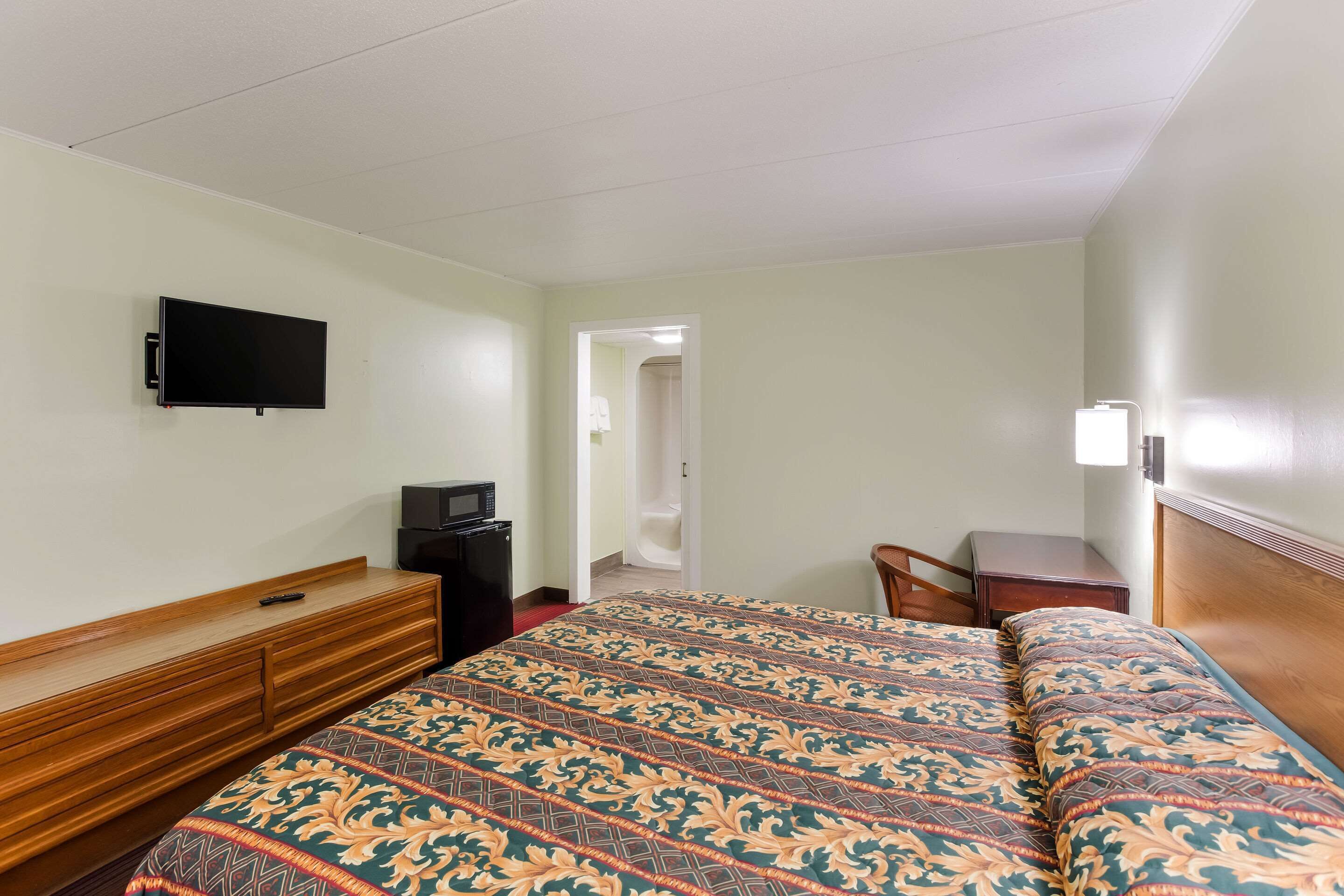 A hotel room with a bed, a TV mounted on the wall, a desk, and a chair.