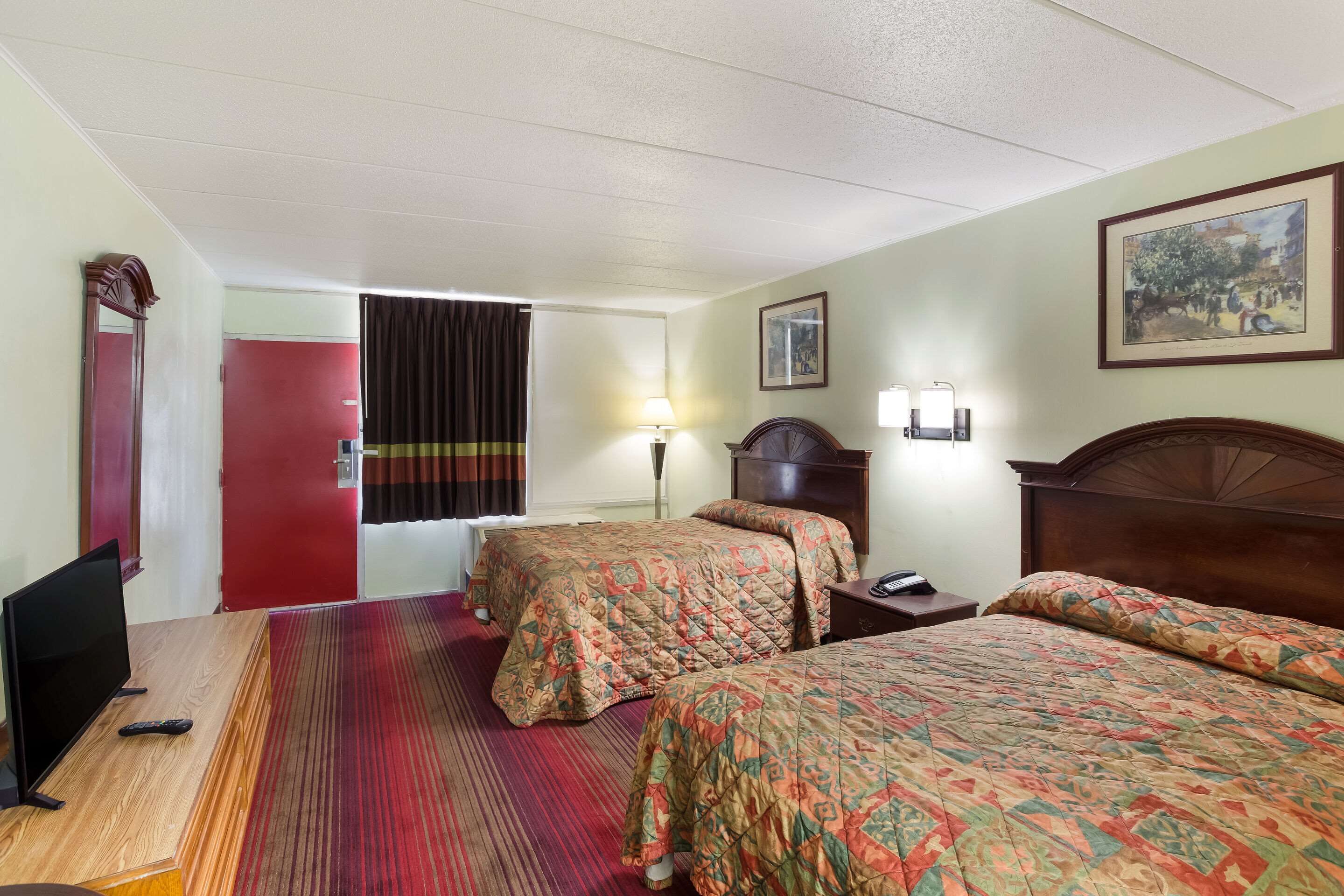 Habitación de hotel con dos camas, televisión, escritorio y una puerta roja.