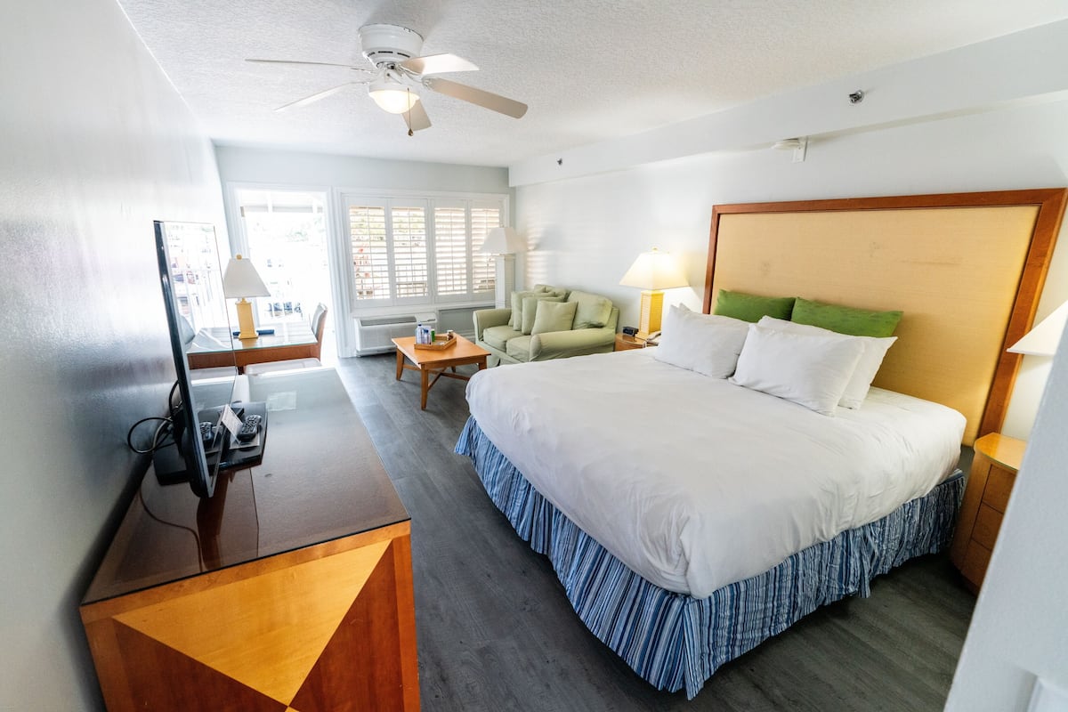 Habitación de hotel con cama, escritorio con computadora, silla, sofá y ventilador de techo.