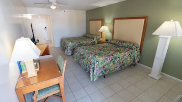 Ein Hotelzimmer mit zwei Betten, einem Schreibtisch mit Stuhl, einem Deckenventilator und zwei Nachttischlampen.