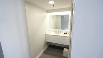 Ein schmaler Flur, der zu einem Badezimmer mit einem weißen Waschbecken, einem Spiegel und Holzböden führt.