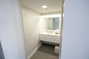A narrow hallway leading to a bathroom with a white sink, mirror, and wooden flooring. - Pirate's Cove Resort & Marina (Stuart)