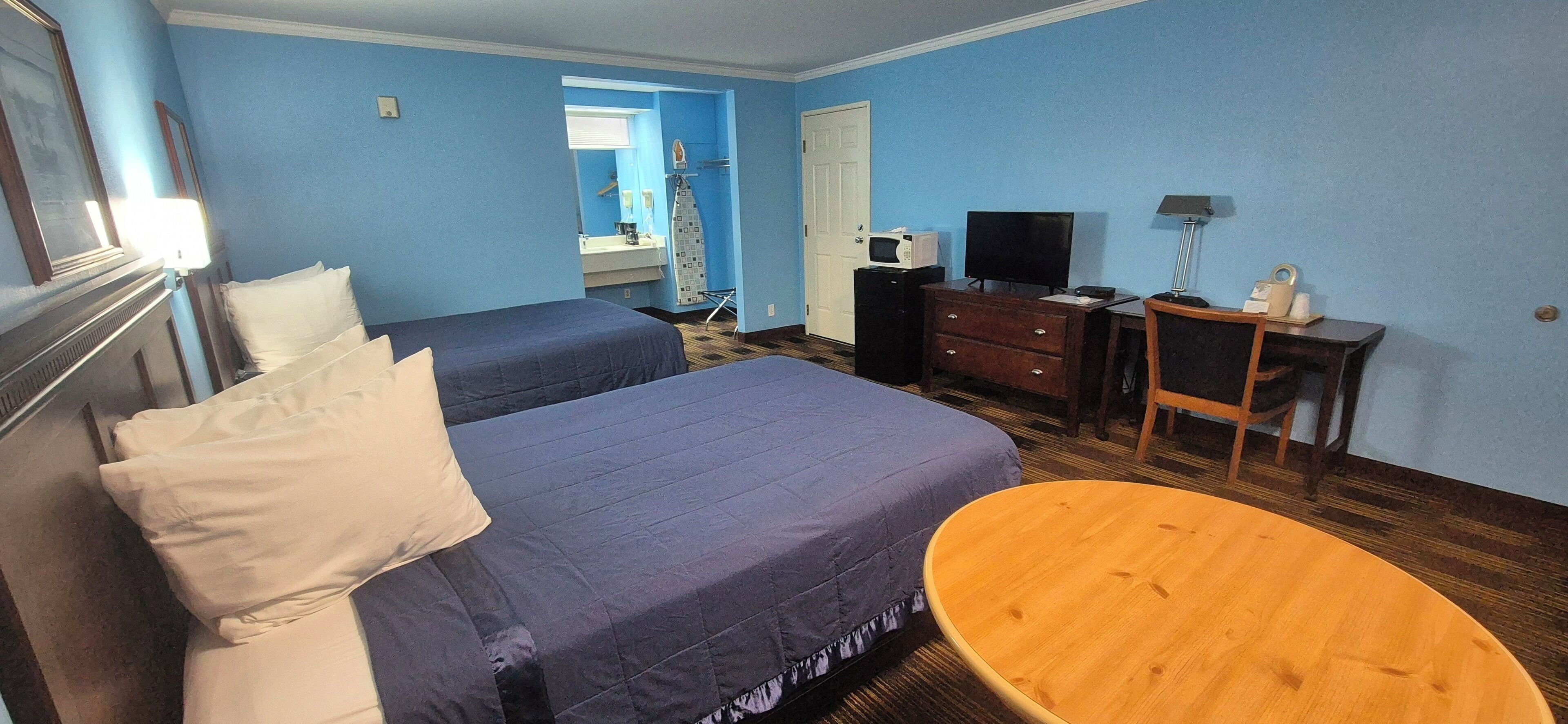Een hotelkamer met twee bedden, een houten tafel, een bureau met een computer, een televisie, en een badkamer zichtbaar door een geopende deur.