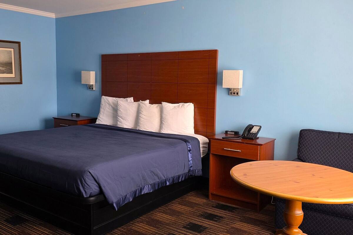 A hotel room with a large bed, bedside tables, a chair, and a small table.