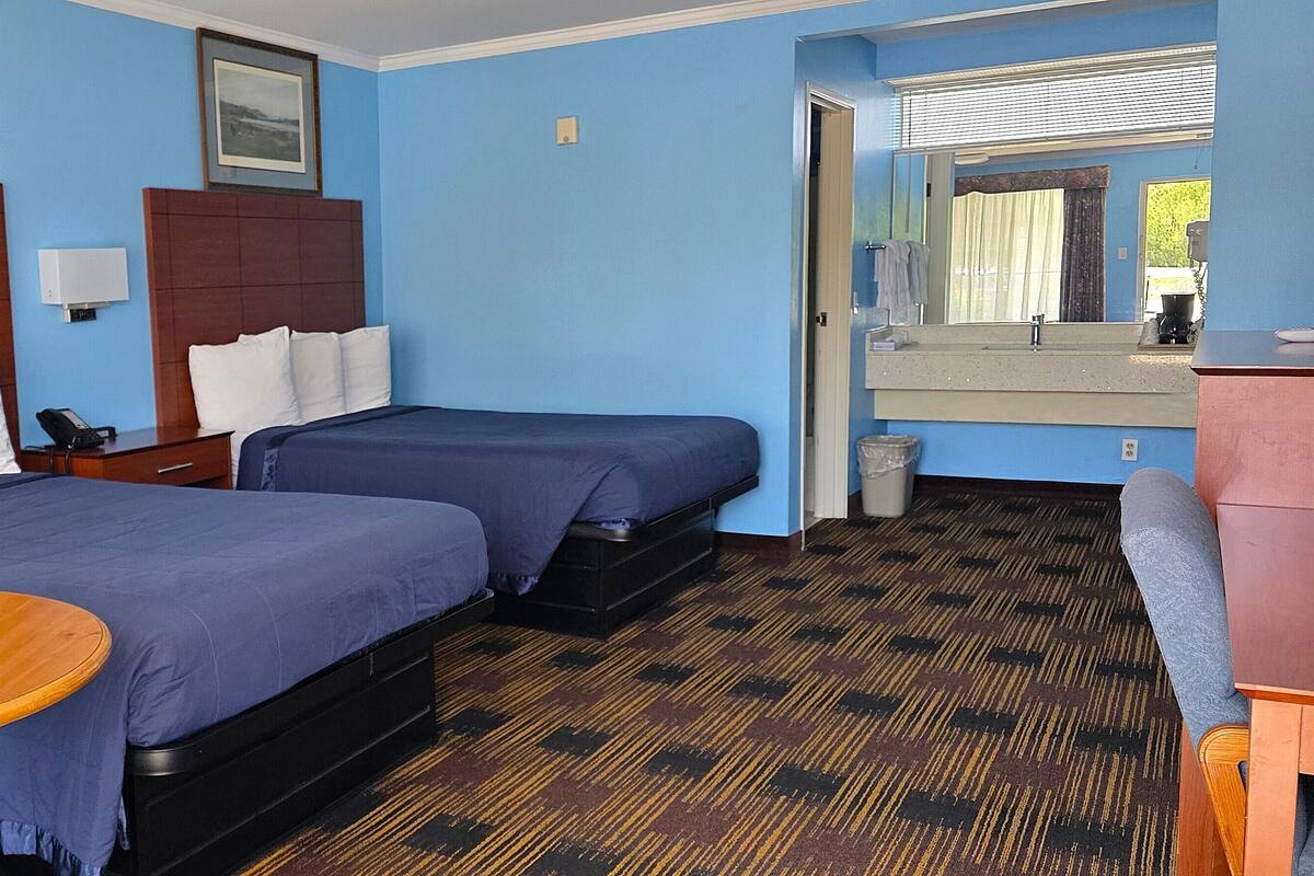 A hotel room with two beds, a wooden table, a mirror, and a patterned carpet.