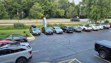 A parking lot with multiple cars parked in designated spaces, surrounded by greenery and a road in the background.