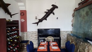 Uma sala de jantar com um piano, um peixe grande montado na parede e uma adega.