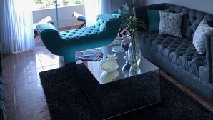 Uma sala de estar com uma poltrona verde-água, um sofá escuro, uma mesa de centro de vidro e um candelabro.