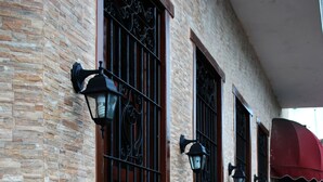 Um edifício com fachada de tijolos, três janelas com grades de metal e um toldo vermelho.