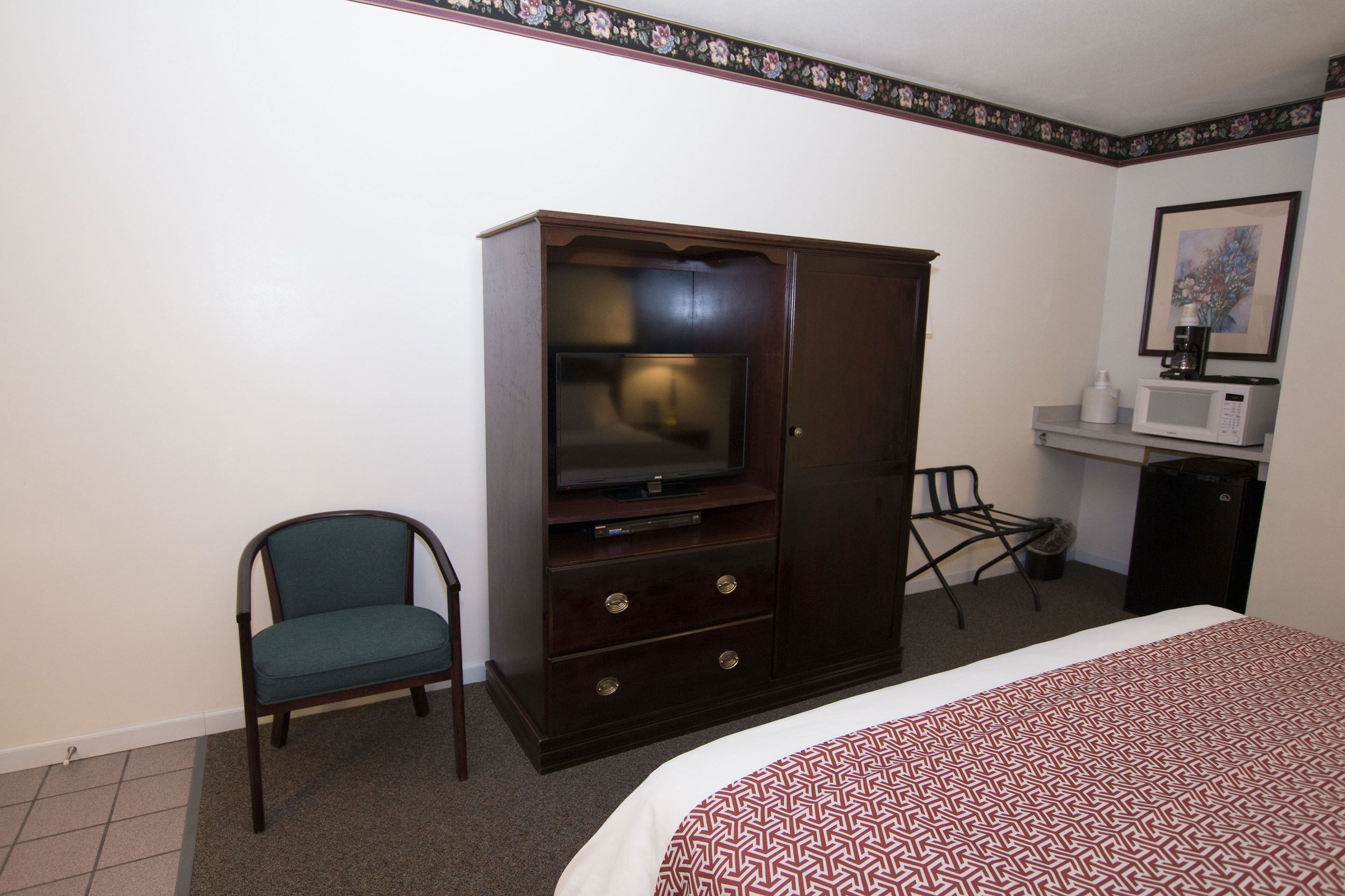 A hotel room with a bed, a television, a small desk, a chair, and a wardrobe.