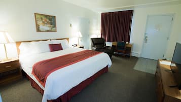 Quarto de hotel com uma cama grande, duas mesas de cabeceira com abajures, uma escrivaninha com cadeira, uma televisão e um quadro na parede.