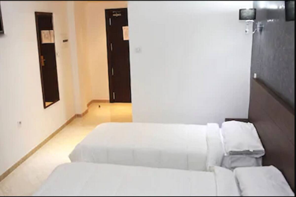 Une chambre d’hôtel avec deux lits, un téléviseur fixé au mur et une porte donnant sur une autre pièce.