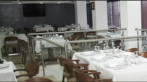 Un restaurante con varias mesas preparadas para comer, una barandilla de cristal que separa el comedor de la cocina, y vista a la cocina a través de la barandilla.