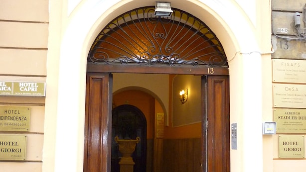 Ein Hotel Eingang mit rotem Teppich, einem Metallgitter und Schildern, die Zimmerverfügbarkeit anzeigen.