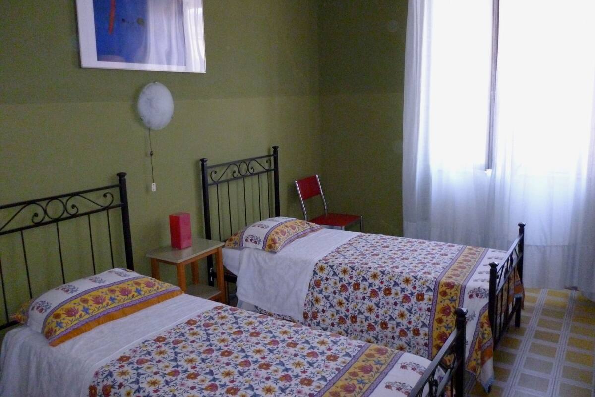 A bedroom with two beds, a chair, a small table, and a window with curtains.