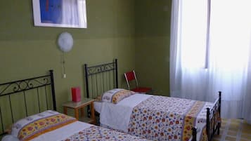 Una camera da letto con due letti, una sedia, un tavolino e una finestra con tende.