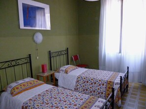 A bedroom with two beds, a chair, a small table, and a window with curtains. - Hotel Giamaica for Girls & Ladies Only (Rome)