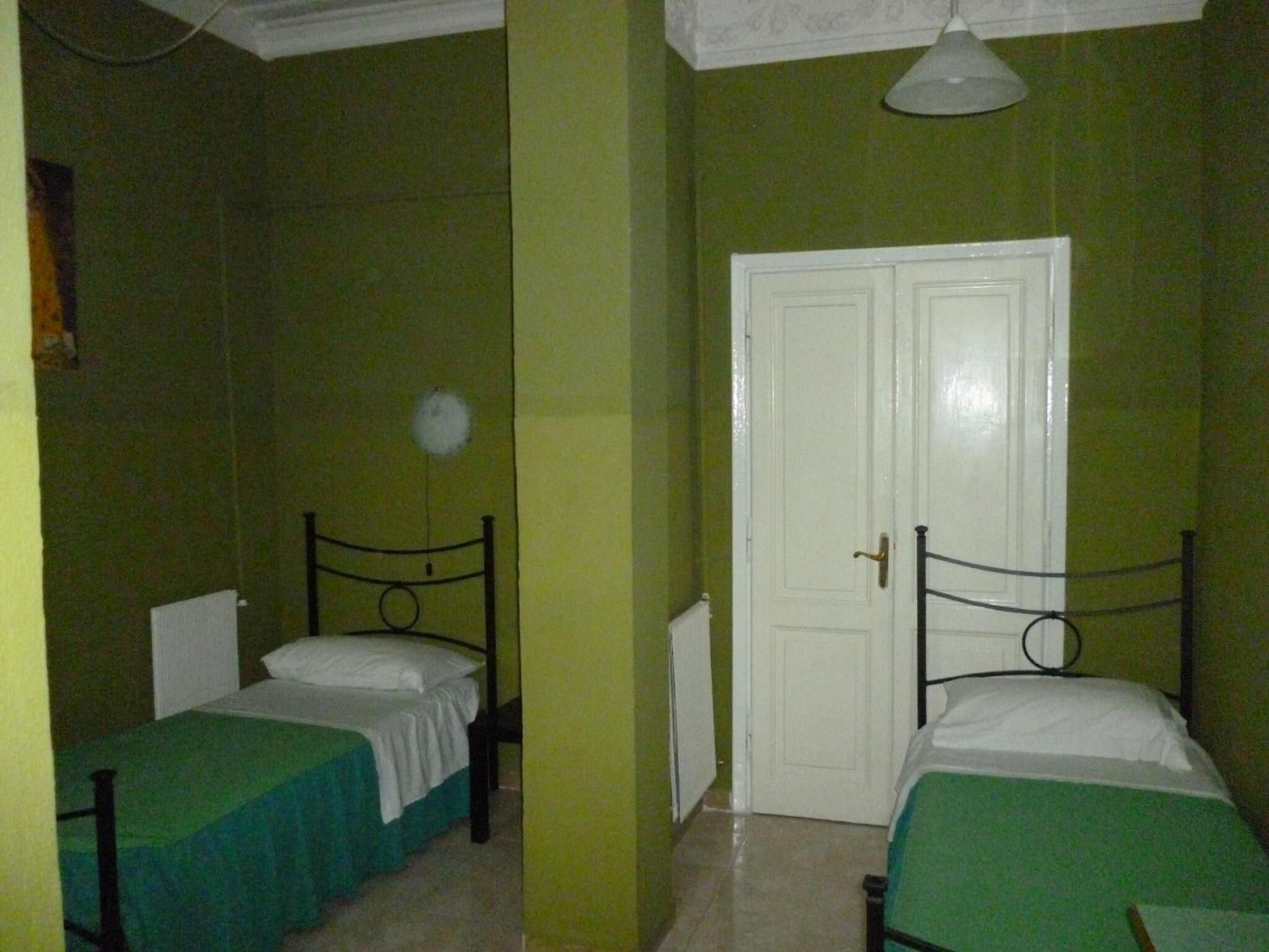 A small room with two single beds, a white door, and green walls.