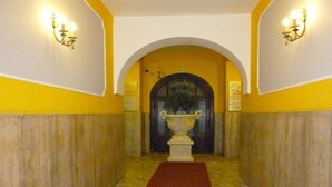 Ein Korridor mit rotem Teppich, gelben Wänden und einem großen, gewölbten Durchgang zu einem Raum mit einer großen Vase.