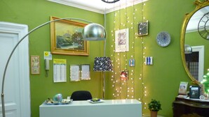 Ein Empfangsschalter mit weißer Theke, einem schwarzen Stuhl und einer Schreibtischlampe. An der Wand befinden sich gerahmte Bilder und eine Uhr.