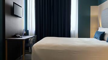 A hotel room with a bed, a desk with a phone, a chair, and a TV on the wall.