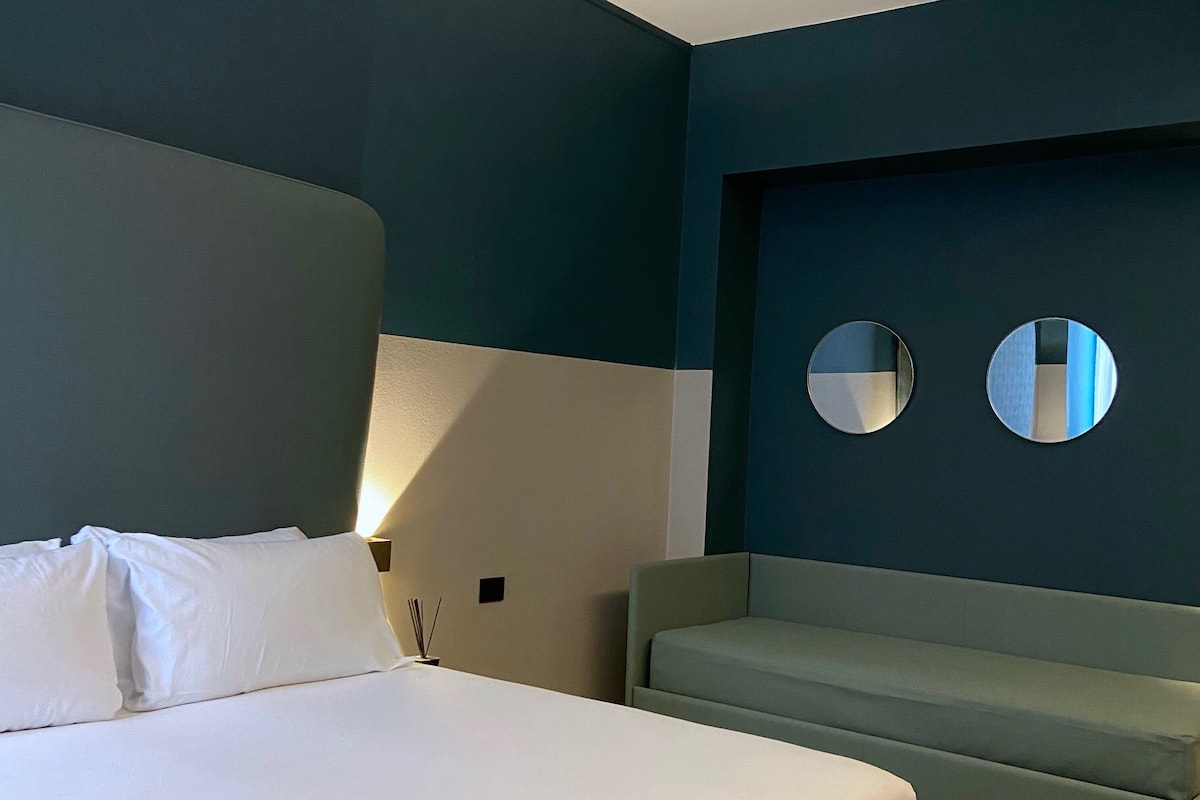A modern hotel room with a large bed, a sofa, and two wall-mounted mirrors.