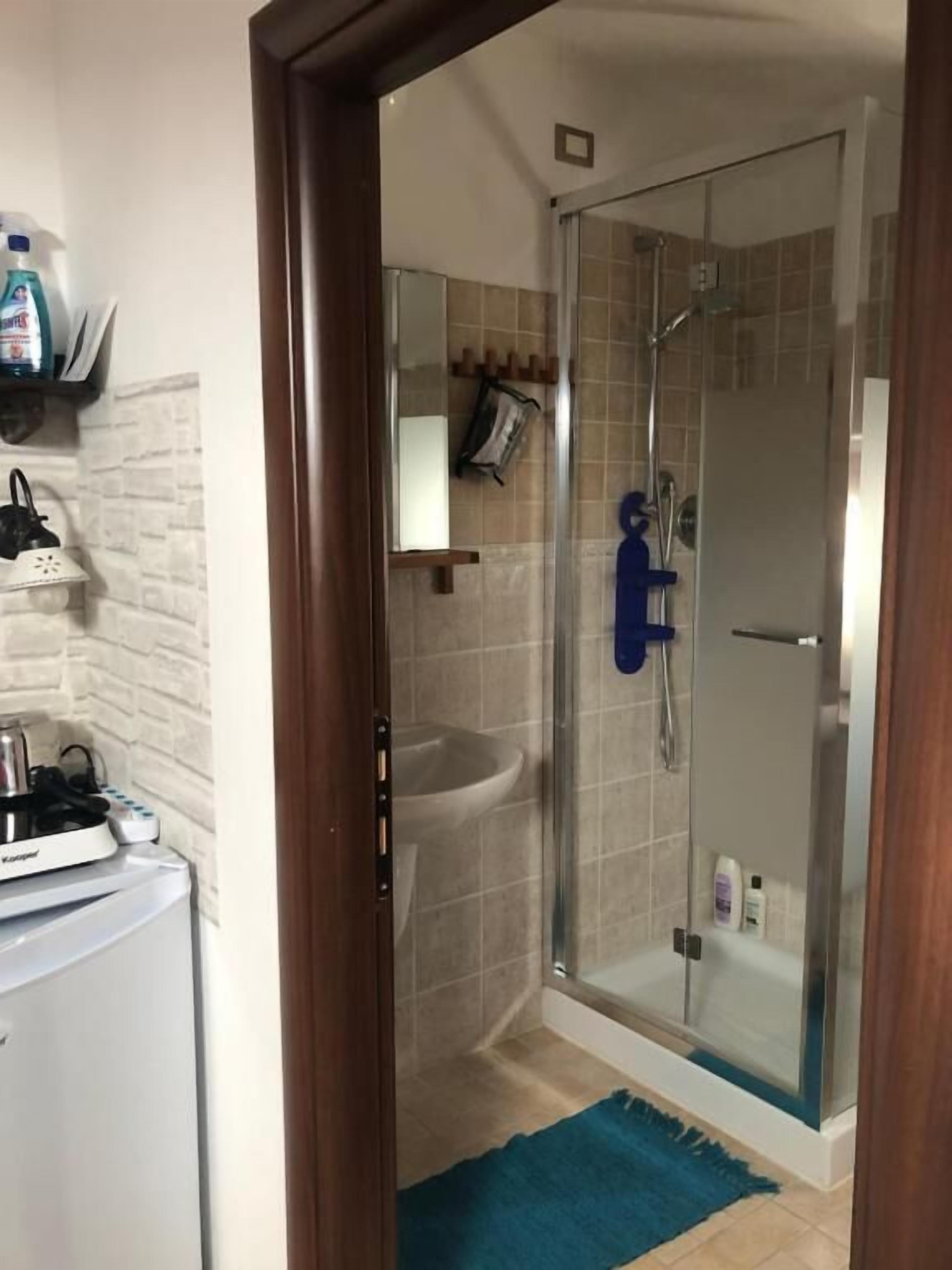 A modern bathroom with a glass shower enclosure, a white sink, and a small countertop with a kettle and other items.