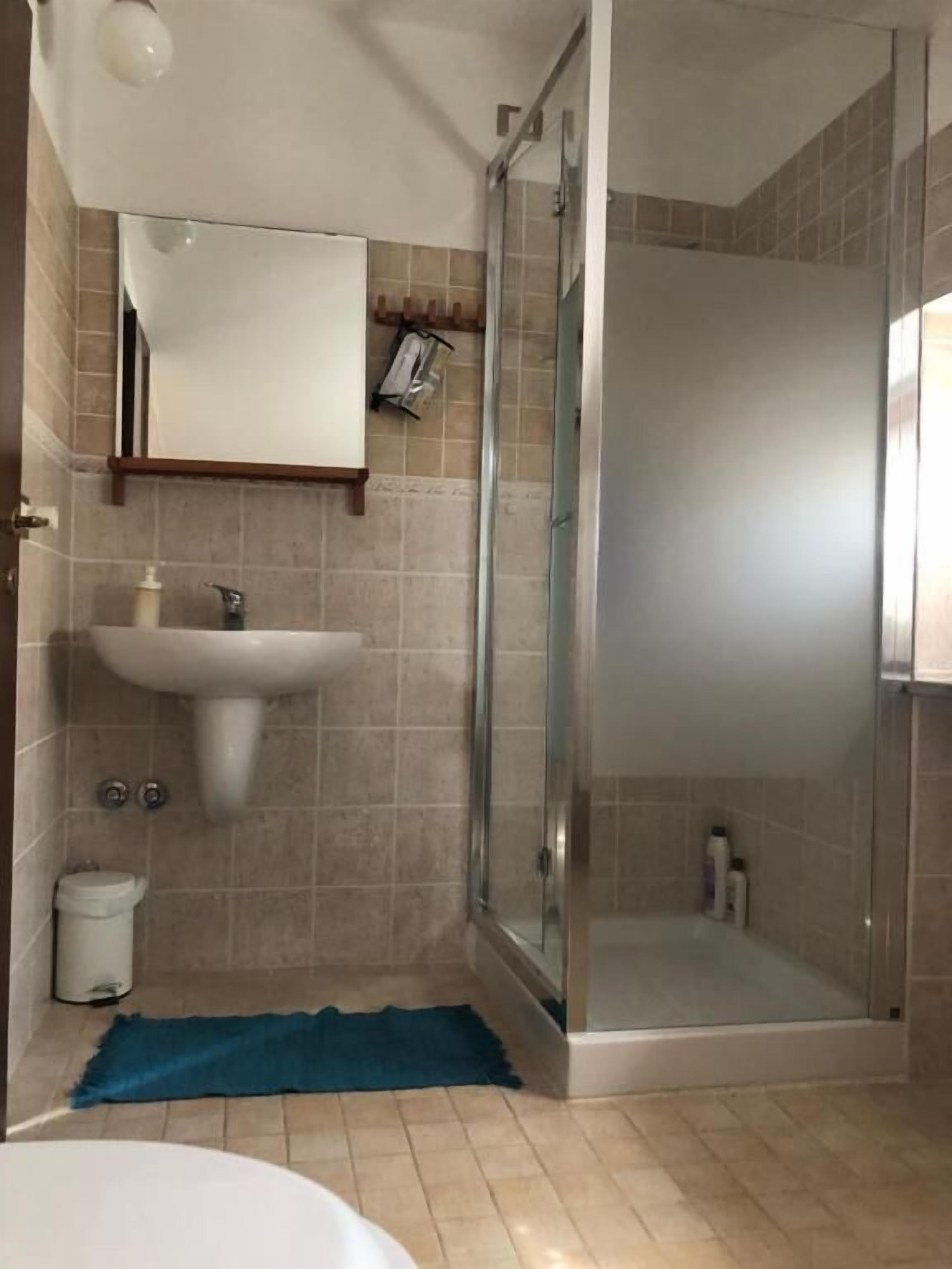 Casa de banho com cabine de chuveiro envidraçada, lavatório e espelho.