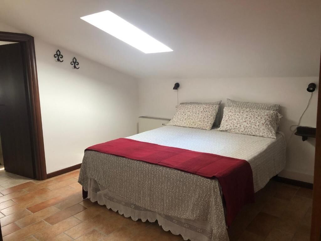 Ein Schlafzimmer mit einem Bett, einer roten Decke, einem Oberlicht und einer Wandleuchte.