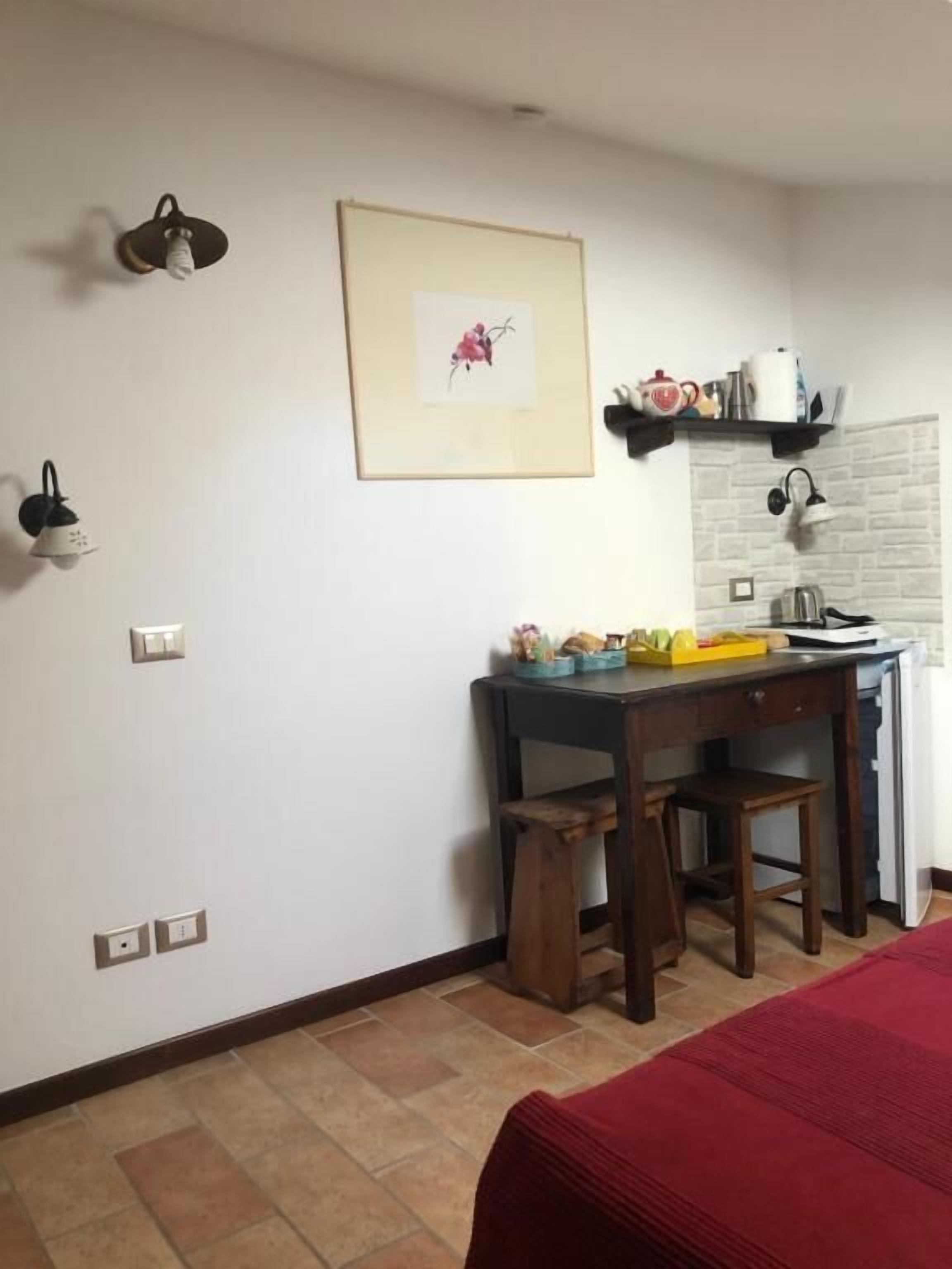 Una habitación pequeña y ordenada con escritorio, silla, cama y estante en la pared con utensilios de cocina.