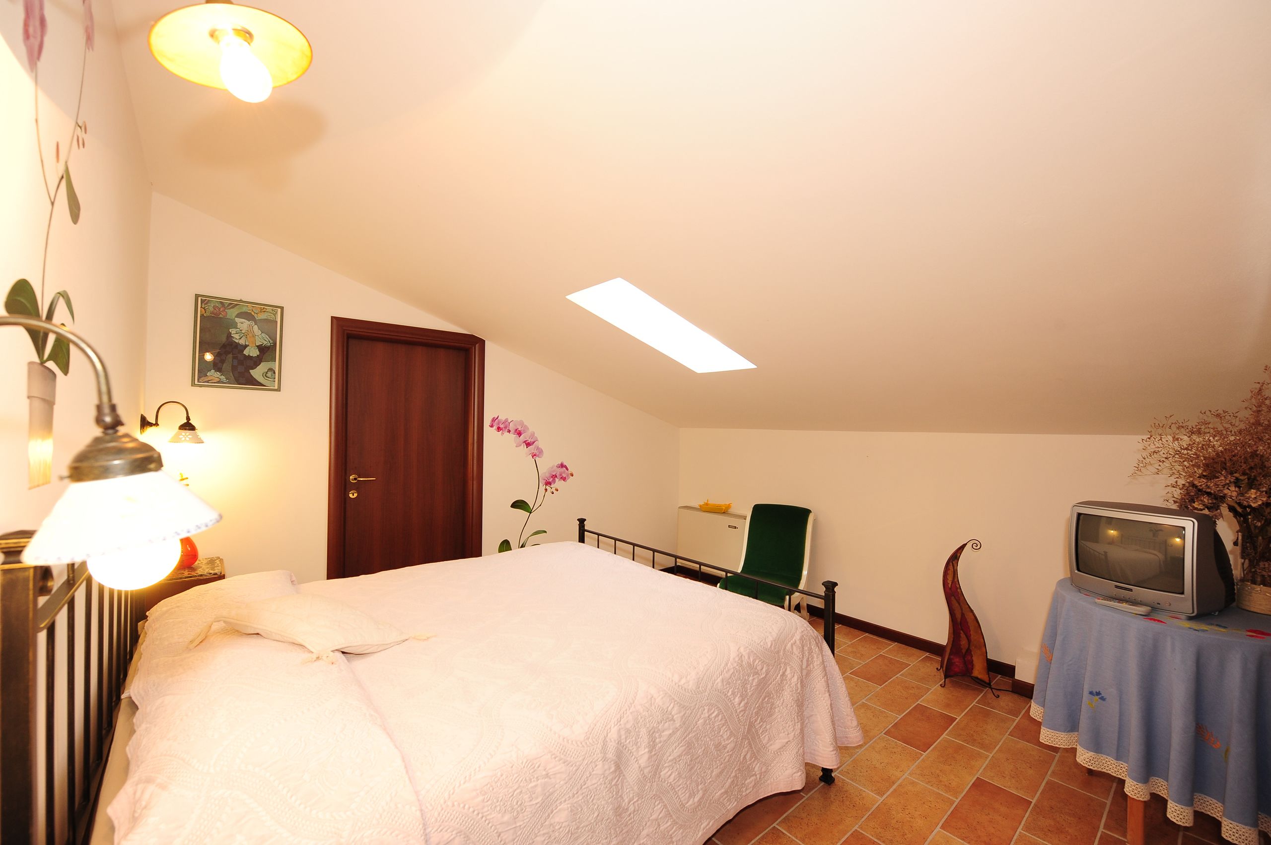 A bedroom with a bed, a desk, a chair, a television, and a radiator.