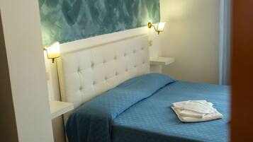 Een slaapkamer met een gestoffeerd hoofdeinde, een blauw sprei en twee wandlampen.