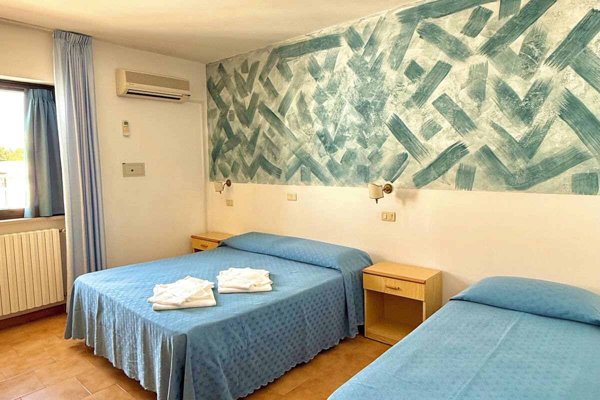 A room with two beds, a radiator, an air conditioning unit, and a patterned wall.