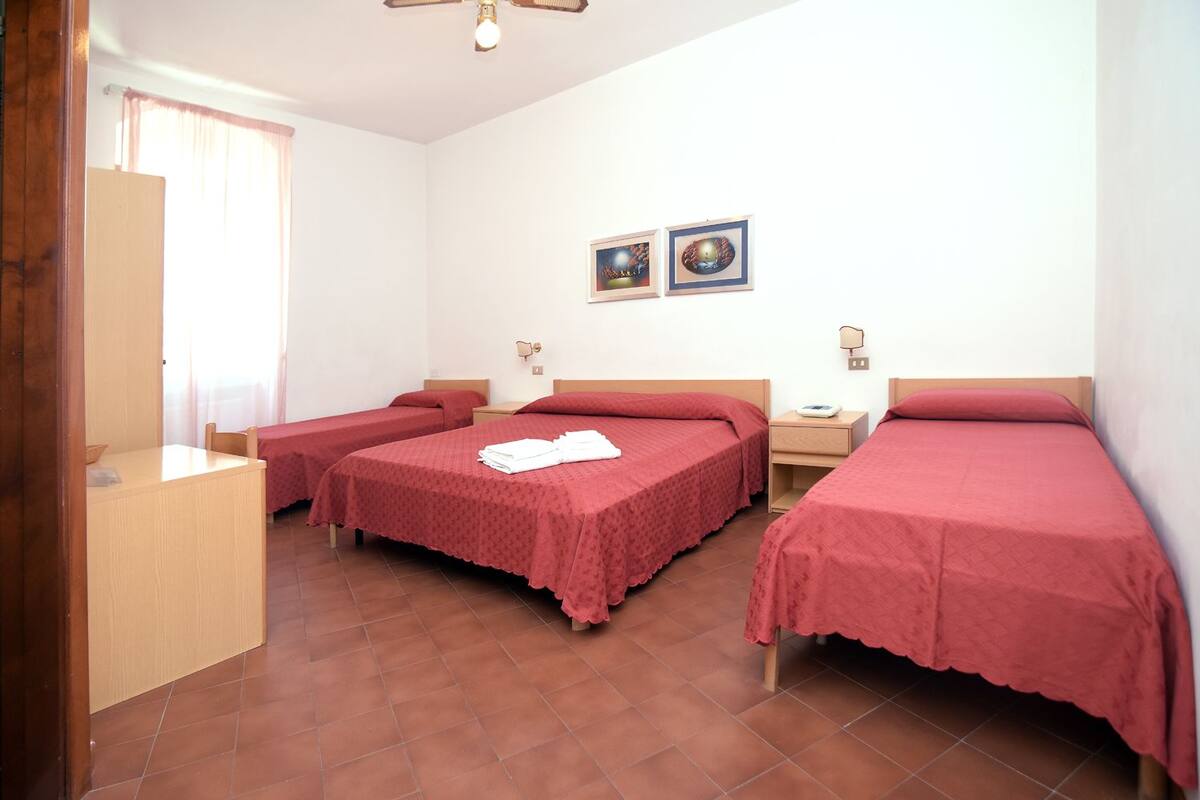 A room with three beds, a wooden desk, and two wall-mounted lamps.