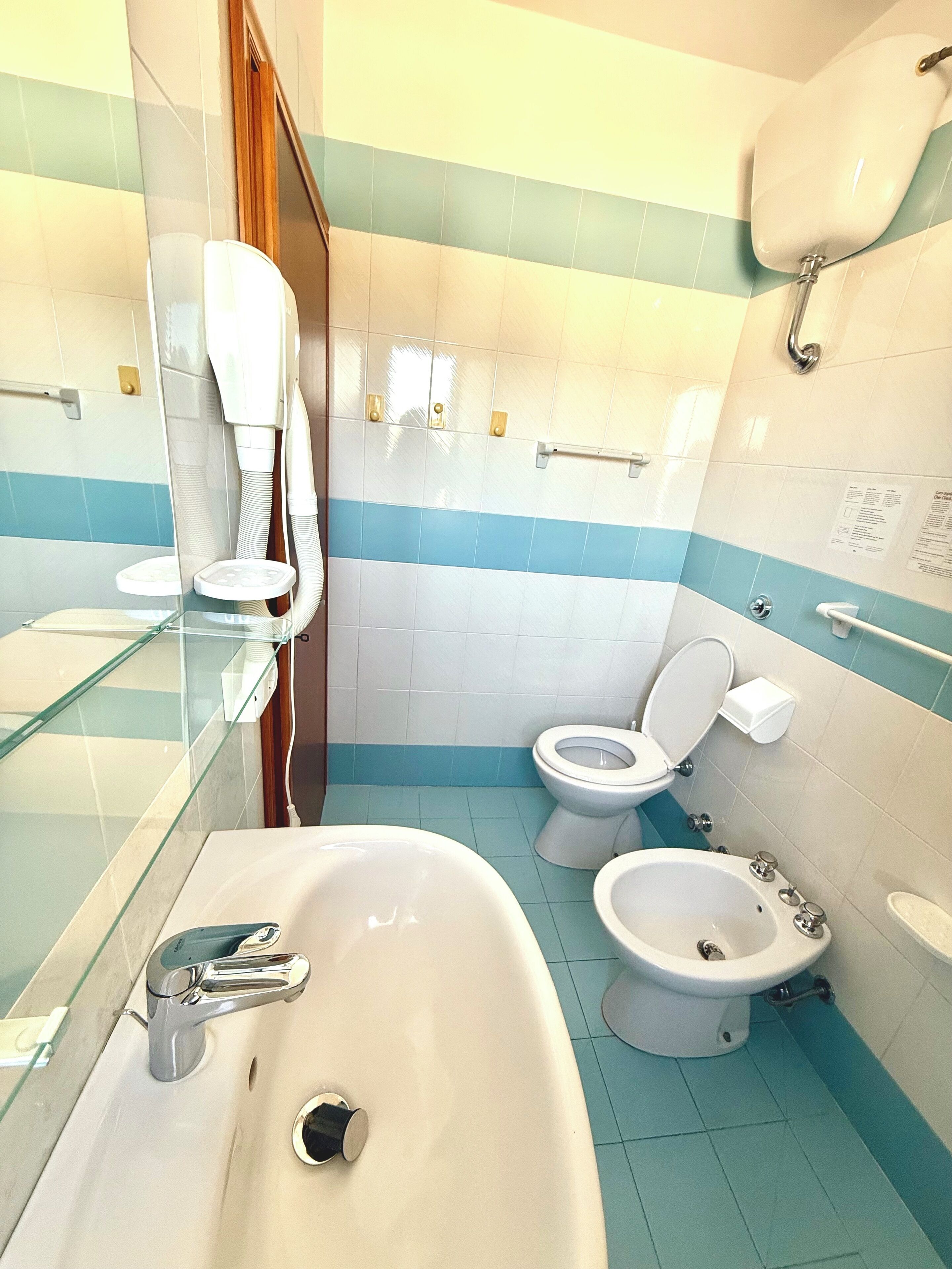A bathroom with a sink, two toilets, a bidet, and a glass shower enclosure.
