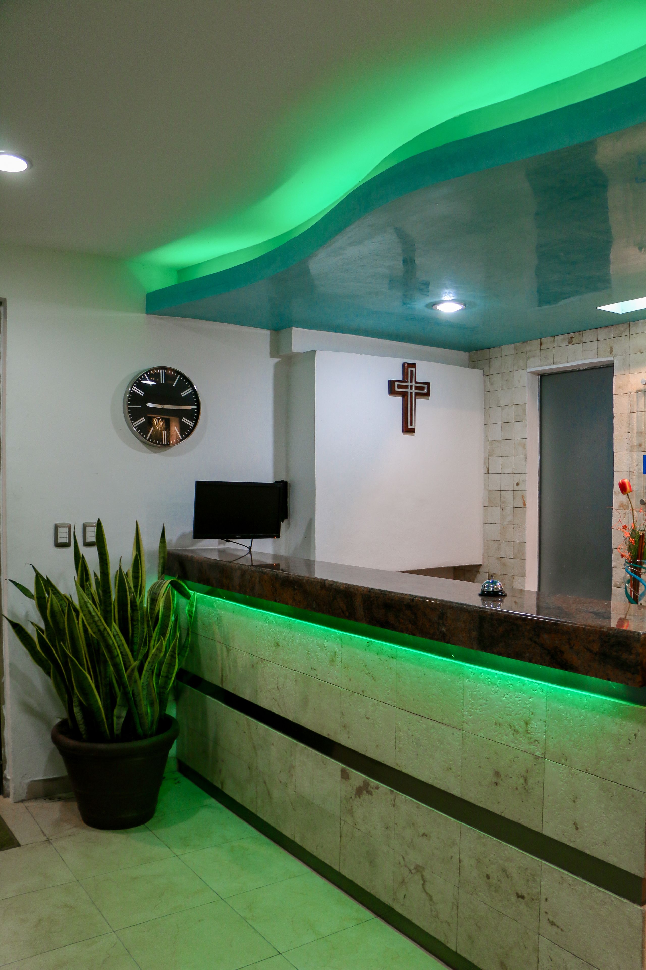 A reception area with a clock, a cross, a TV, and a potted plant.