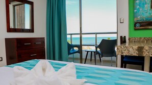 Una habitación de hotel con cama, escritorio, silla, ventana con vista al mar y un cuadro en la pared.