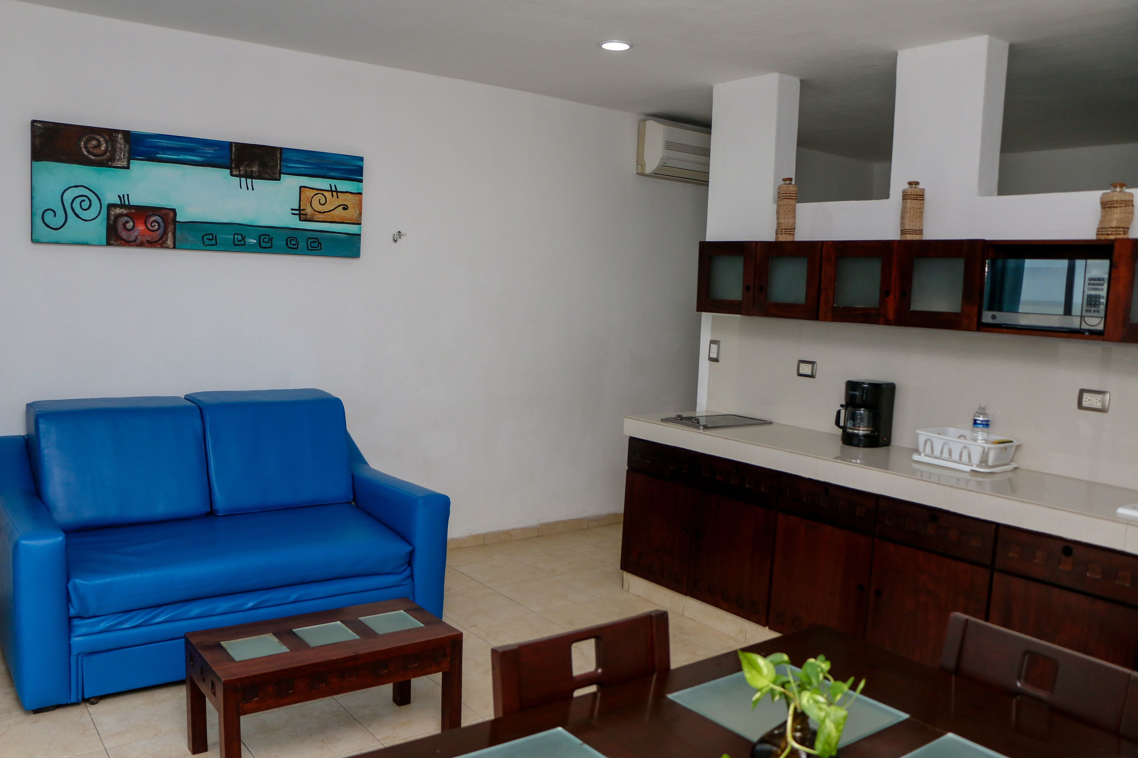 A living room with a blue sofa, wooden coffee table, and a dining area with a table and chairs.