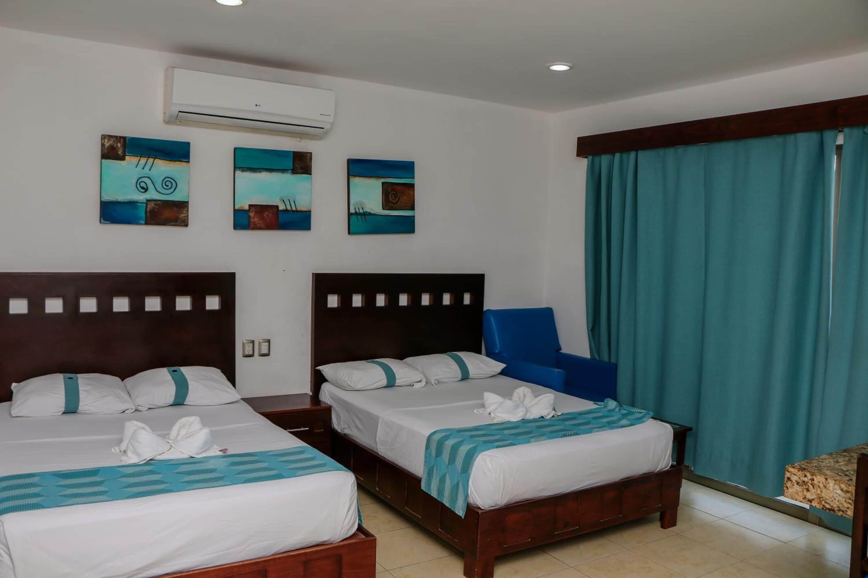A hotel room with two beds, a blue chair, and artwork on the wall.